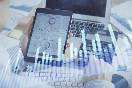 Double exposure of man's hands holding and using a digital device and forex graph drawing. Financial...