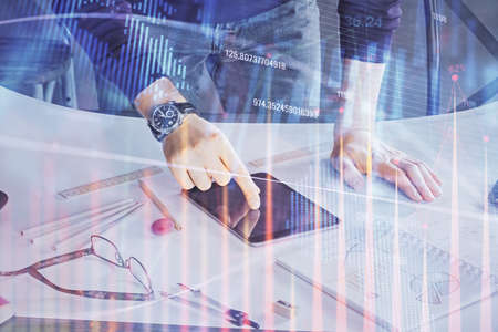 Double exposure of man's hands holding and using a digital device and forex graph drawing. Financial...