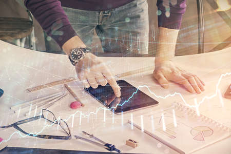 Double exposure of man's hands holding and using a digital device and forex graph drawing. Financial...