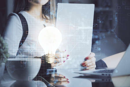 Bulb hologram over hands taking notes background. Concept of idea. Double exposure