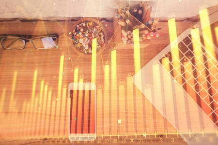 Double exposure of financial graph hologram over desktop with phone. Top view. Mobile trade platform...