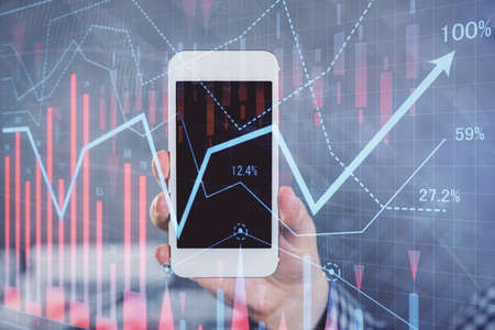 Double exposure of man's hands holding and using a digital device and forex graph drawing. Financial...