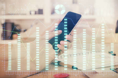 Double exposure of man's hands holding and using a digital device and forex graph drawing. Financial...