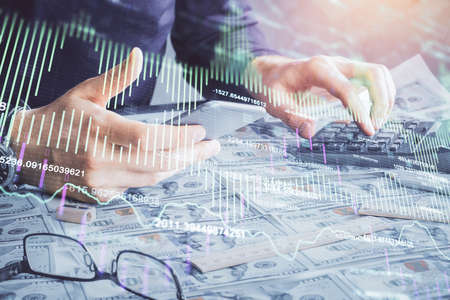 Double exposure of man's hands holding and using a digital device and forex graph drawing. Financial...