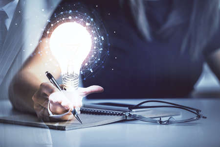 Bulb hologram over hands taking notes background. Concept of idea. Double exposure