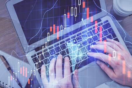 Double exposure of man's hands typing over computer keyboard and forex graph hologram drawing. Top...