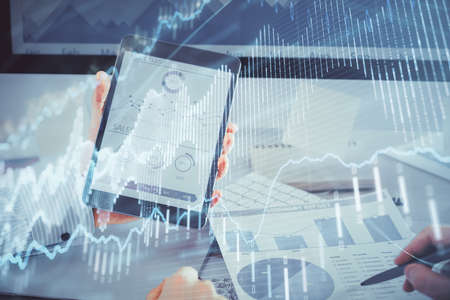 Double exposure of man's hands holding and using a digital device and forex graph drawing. Financial...