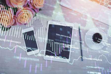 Double exposure of forex graph hologram over desktop with phone. Top view. Mobile trade platform...