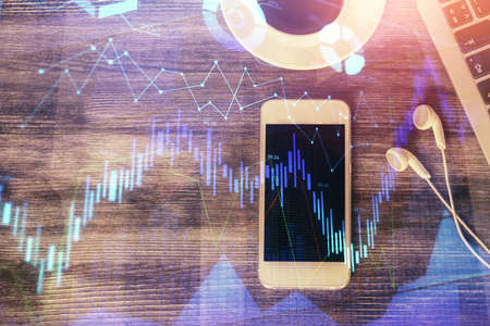 Double exposure of forex chart hologram over desktop with phone. Top view. Mobile trade platform...