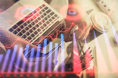 Double exposure of businesswoman hands typing on computer and financial graph hologram drawing....