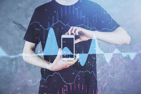 Double exposure of man's hands holding and using a digital device and forex graph drawing. Financial...