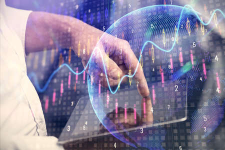Double exposure of man's hands holding and using a digital device and forex graph drawing. Financial...
