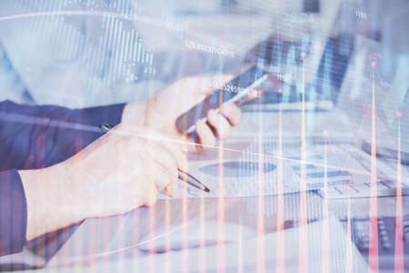 Double exposure of man's hands holding and using a digital device and forex graph drawing. Financial...