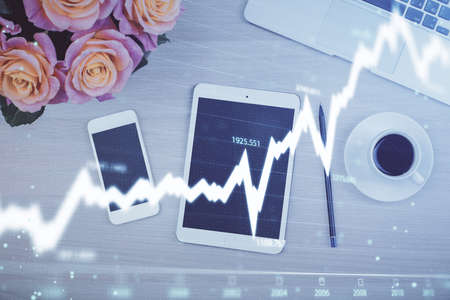 Double exposure of forex graph hologram over desktop with phone. Top view. Mobile trade platform...