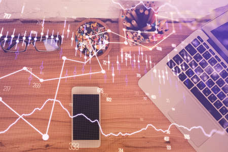 Double exposure of financial graph hologram over desktop with phone. Top view. Mobile trade platform...