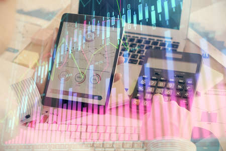 Double exposure of man's hands holding and using a digital device and forex graph drawing. Financial market concept.の写真素材