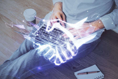 Handshake hologram drawing with businessman working on computer on background. Double exposure.の写真素材