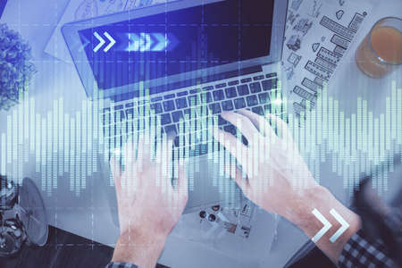 Double exposure of mans hands typing over laptop keyboard and forex chart hologram drawing. Top...