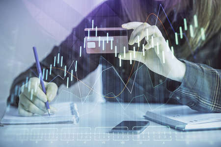 Double exposure of woman on-line shopping holding a credit card and financial graph drawing. Stock...
