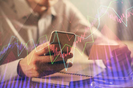 Double exposure of man hands holding and using a phone and financial graph drawing. Analysis...