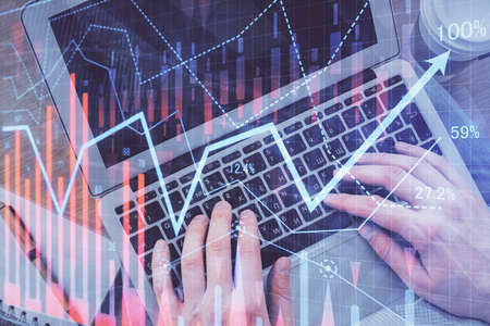 Double exposure of mans hands typing over computer keyboard and forex graph hologram drawing. Top...