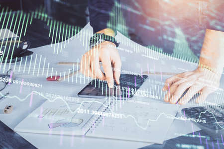 Double exposure of mans hands holding and using a digital device and forex graph drawing. Financial...