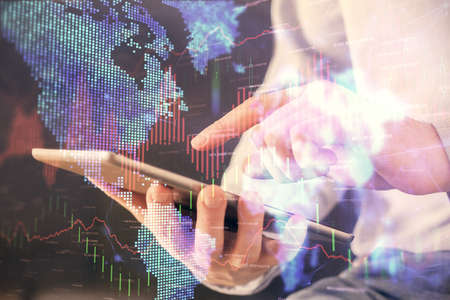 Double exposure of mans hands holding and using a digital device and forex graph drawing. Financial...