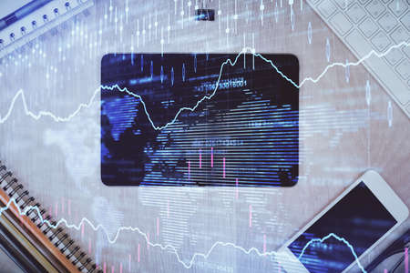 Double exposure of forex graph hologram over desktop with phone. Top view. Mobile trade platform...