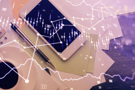 Multi exposure of forex graph hologram over desktop with phone. Top view. Mobile trade platform...
