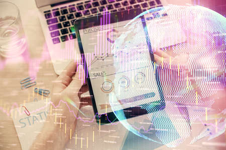 Double exposure of mans hands holding and using a digital device and forex graph drawing. Financial...