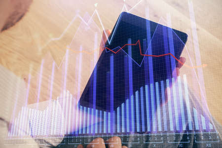 Double exposure of mans hands holding and using a digital device and forex graph drawing. Financial...