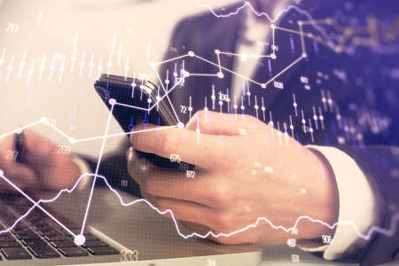 Multi exposure of mans hands holding and using a digital phone and forex graph drawing. Financial...