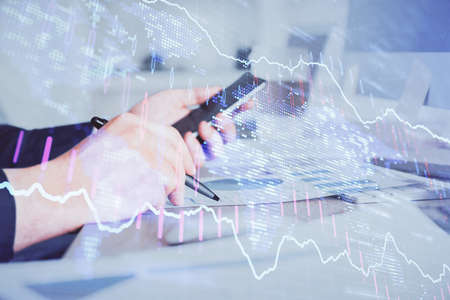 Double exposure of mans hands holding and using a phone and financial graph drawing. Analysis...