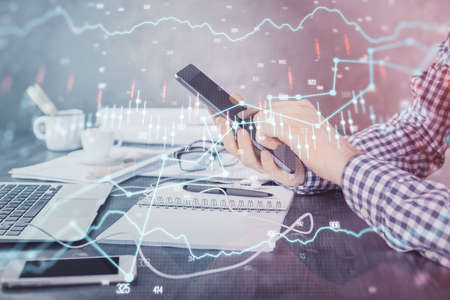 Double exposure of mans hands holding and using a digital device and forex graph drawing. Financial market concept.の写真素材