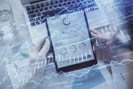 Double exposure of mans hands holding and using a digital device and forex graph drawing. Financial...