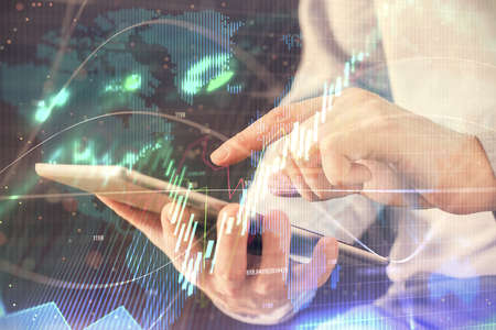 Double exposure of mans hands holding and using a digital device and forex graph drawing. Financial...