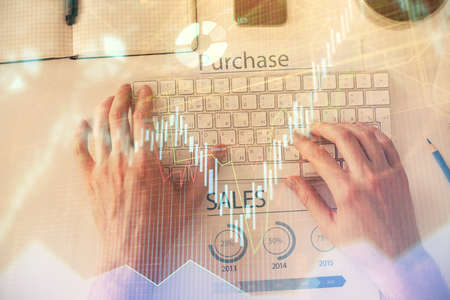 Double exposure of mans hands typing over computer keyboard and forex graph hologram drawing. Top view. Financial markets concept.の写真素材