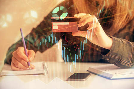 Double exposure of woman on-line shopping holding a credit card and financial graph drawing. Stock market E-commerce concept.の写真素材