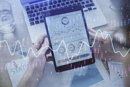 Double exposure of mans hands holding and using a digital device and forex graph drawing. Financial...
