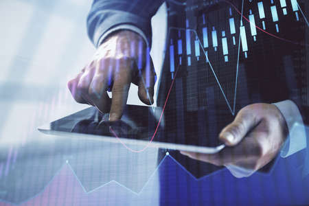 Double exposure of mans hands holding and using a digital device and forex graph drawing. Financial market concept.の写真素材