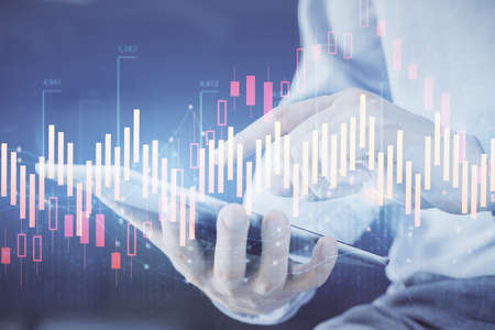 Double exposure of mans hands holding and using a digital device and forex graph drawing. Financial...