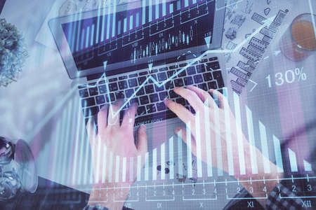 Double exposure of mans hands typing over laptop keyboard and forex chart hologram drawing. Top...