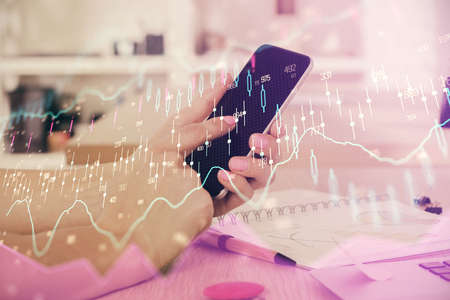 Double exposure of mans hands holding and using a digital device and forex graph drawing. Financial...