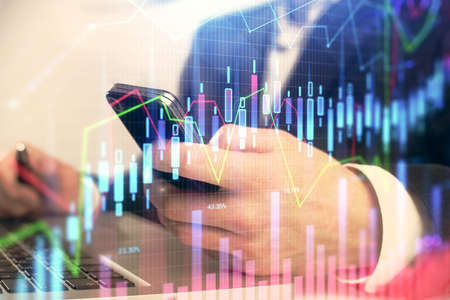 Multi exposure of mans hands holding and using a digital phone and forex graph drawing. Financial...