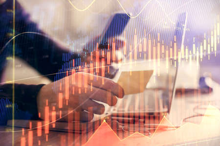 Double exposure of mans hands holding and using a phone and financial graph drawing. Analysis...