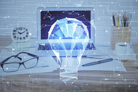 Computer on desktop in office with bulb icon hologram. Double exposure. Concept of idea.