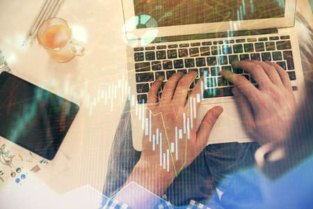 Double exposure of mans hands typing over laptop keyboard and forex chart hologram drawing. Top...