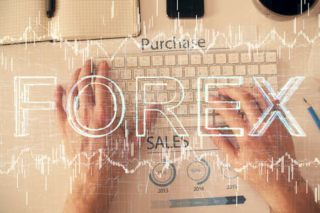 Double exposure of mans hands typing over computer keyboard and forex graph hologram drawing. Top...