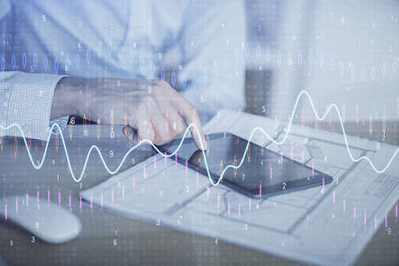 Double exposure of mans hands holding and using a digital device and forex graph drawing. Financial...