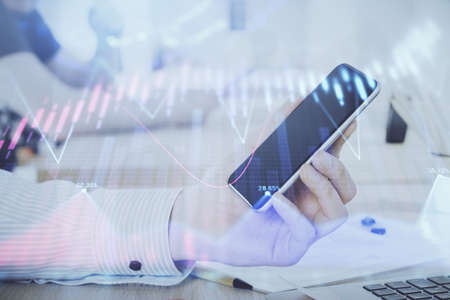 Double exposure of mans hands holding and using a digital device and forex graph drawing. Financial...